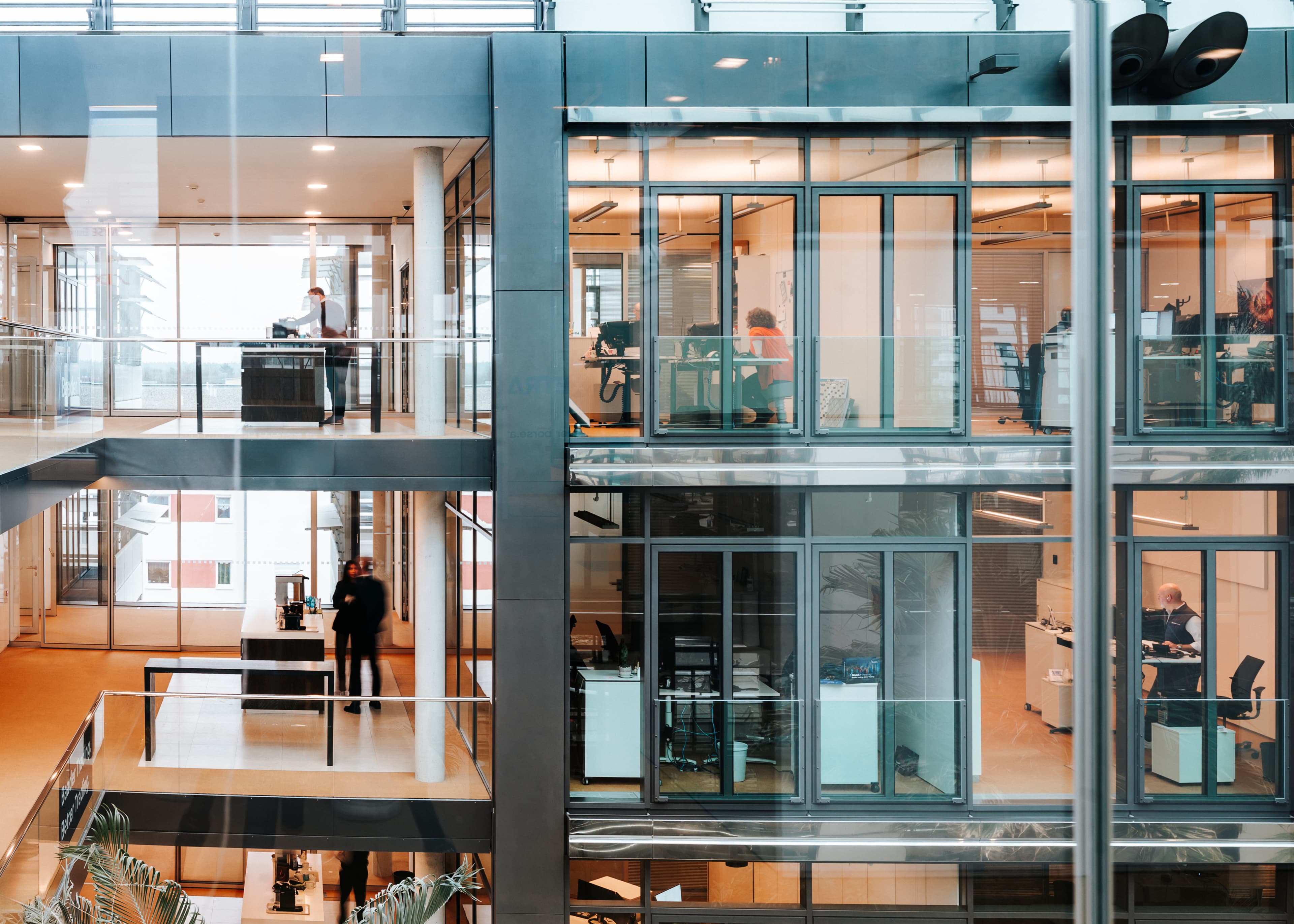 Innenansicht des modernen Baaderbank Bürogebäudes mit Glasfronten und Mitarbeitenden an Schreibtischen.