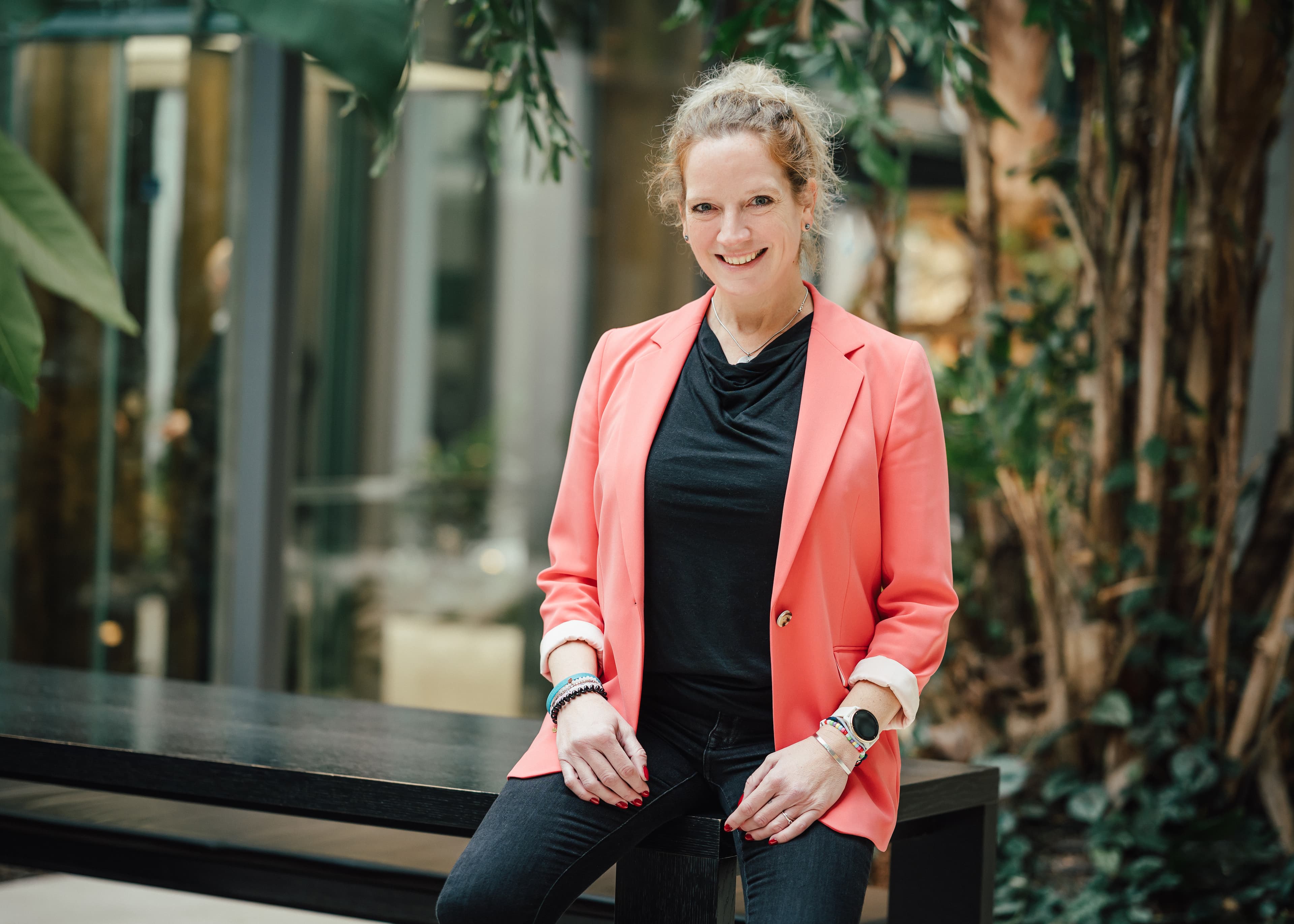 Porträt einer Frau im Business-Outfit, aufgenommen in einem begrünten Innenbereich.