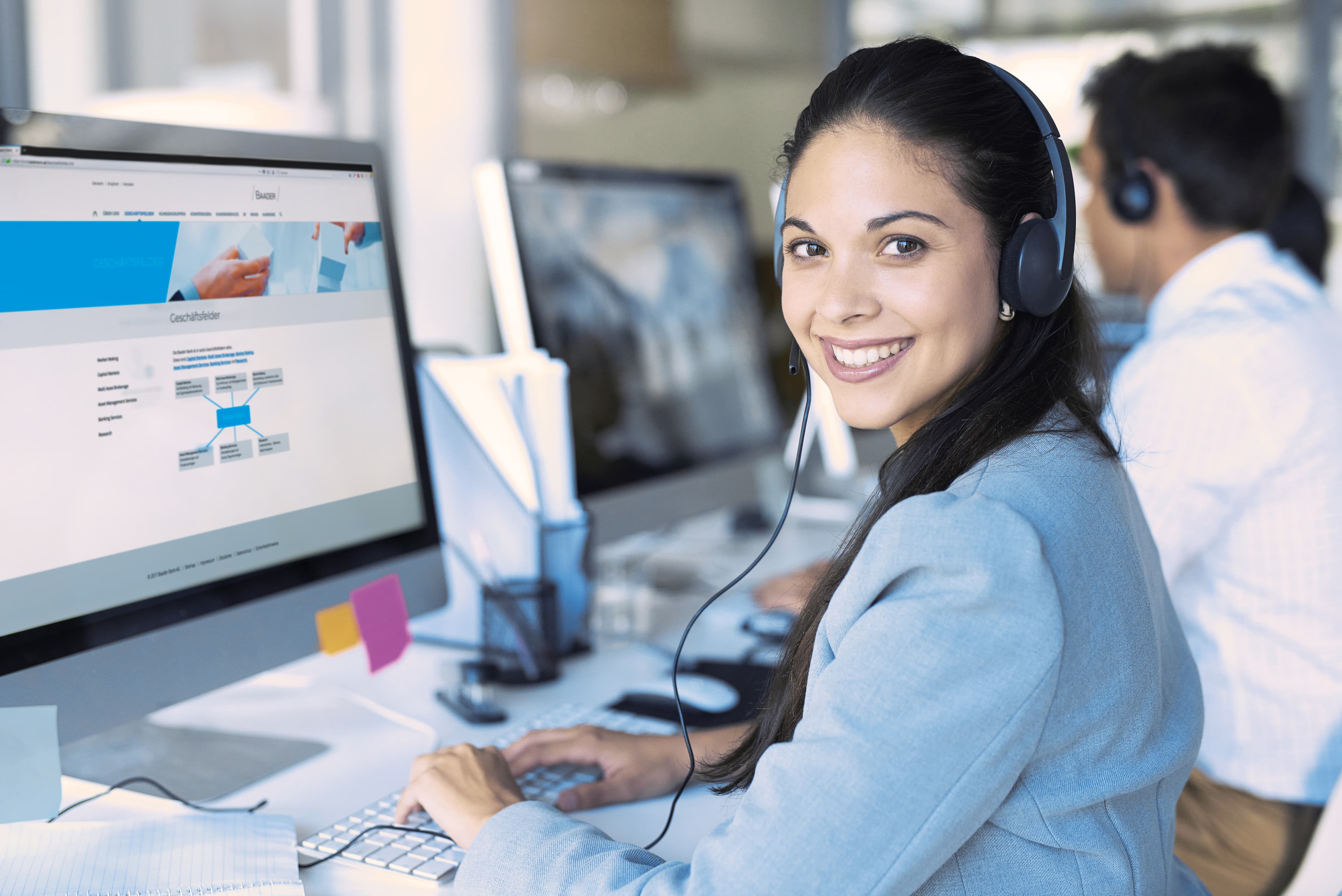 Freundliche Baaderbank Mitarbeiterin im Kundenservice mit Headset am Computer.