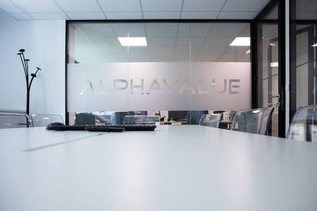 Konferenzraum mit Glaswand und Schriftzug Alphavalue, Blick auf Bürostühle und Tisch.