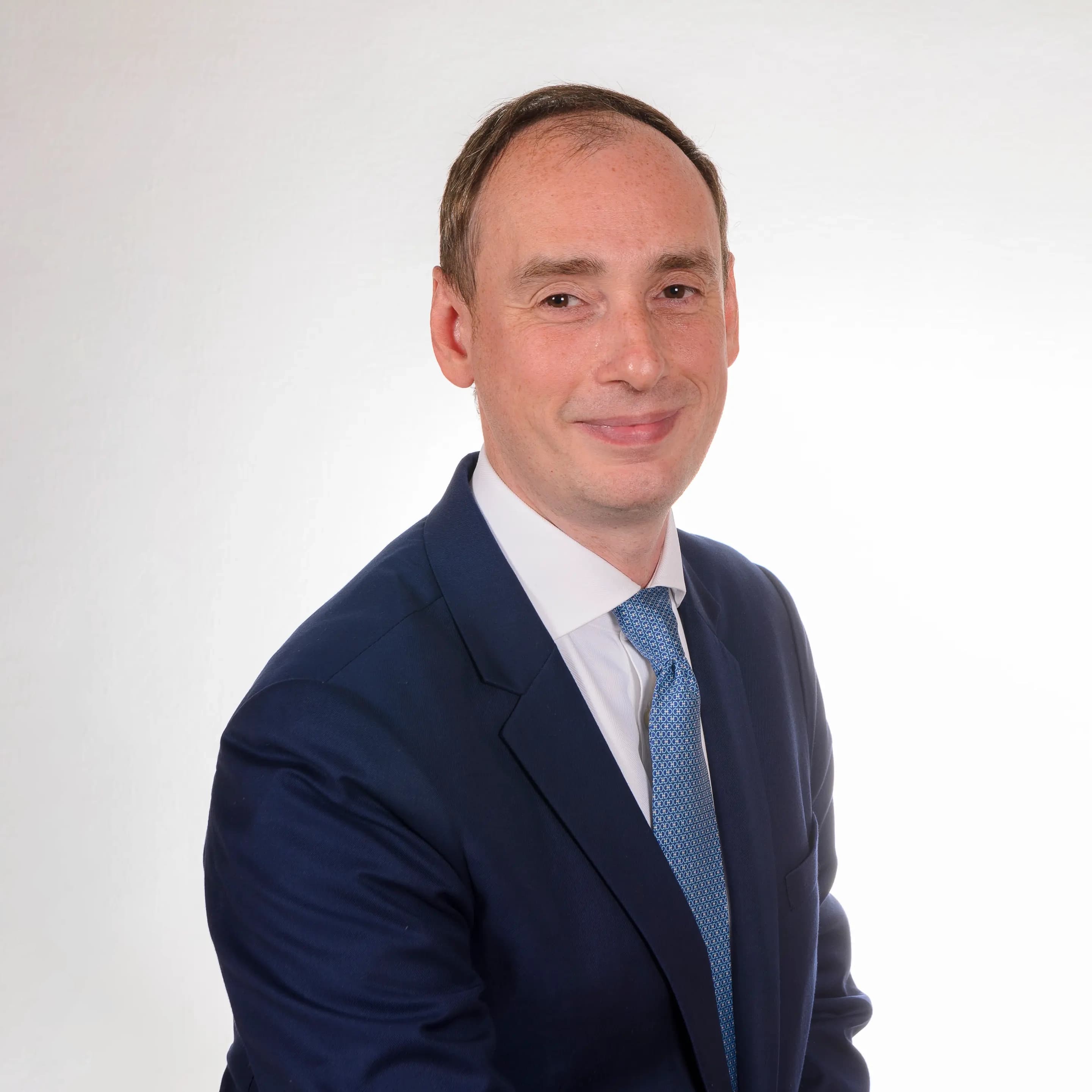 Porträt eines Mannes im blauen Anzug mit Krawatte vor hellem Hintergrund.